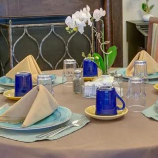 A neatly arranged dining table with folded napkins, blue mugs, and an orchid centerpiece.