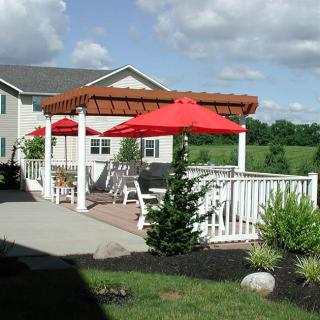 A cozy outdoor patio with red umbrellas and a pergola next to a house.