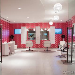 A modern hair salon with pink patterned walls, stylish chairs, and mirrors.