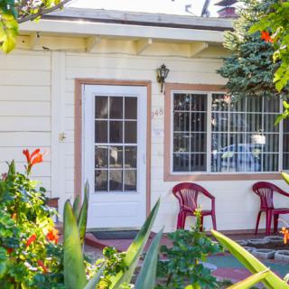 A cozy garden patio with chairs, surrounded by lush greenery and flowers.