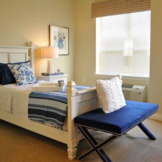 A well-decorated bedroom with a neatly made bed, blue accents, and natural lighting.