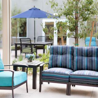 A cozy outdoor seating area featuring comfortable striped furniture and a pop of blue from an umbrella.