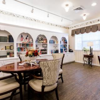 A cozy reading room with a round table and chairs, surrounded by built-in bookshelves filled with books and decorative items.