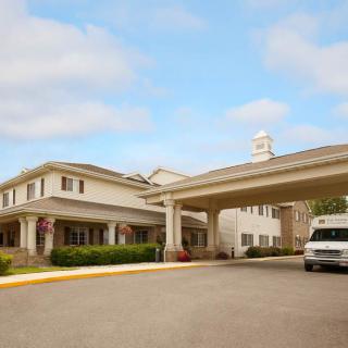 A building with an entrance canopy and a vehicle parked in front under a partly cloudy sky.
