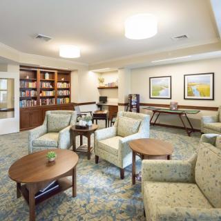 A cozy living room area with comfortable chairs, a central table, bookshelves, and warm lighting.