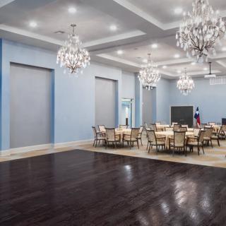 An elegant banquet hall with chandeliers, round tables, and a polished wooden floor.