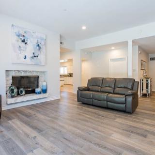 A modern living room with a leather couch, fireplace, and wood flooring, featuring minimalist decor and artwork.