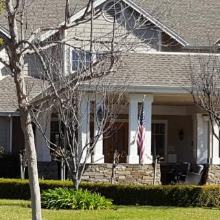 A suburban house with a front porch and well-maintained yard, featuring trees and shrubs.