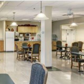 A well-lit dining area with tables and chairs, adjacent to a kitchen space.