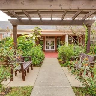A peaceful garden pathway with benches and lush greenery under a pergola.