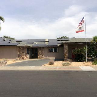 A single-story house with solar panels on the roof, an American flag in the yard, and a well-maintained driveway.
