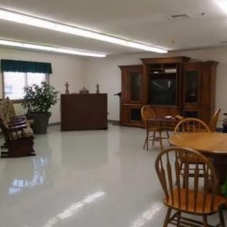 A living room with wooden furniture, including a table and chairs, a large cabinet, and a potted plant.