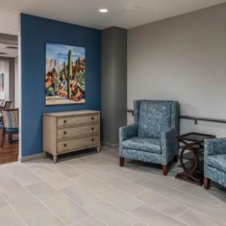 A modern waiting area featuring two blue armchairs, a small dresser, and a colorful painting on the wall.
