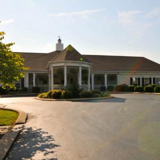 A large building with a circular driveway, surrounded by greenery under a sunny sky.