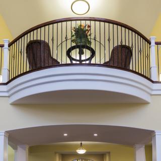 An interior balcony with a decorative railing, featuring two chairs and a small table with a plant.