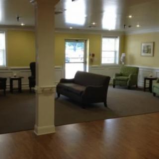 A cozy living area with sofas and chairs arranged around a carpeted floor, featuring large windows and a doorway.