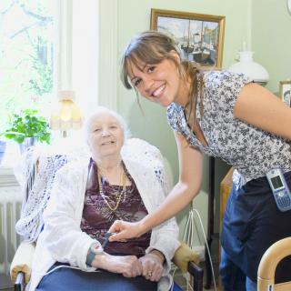 A nurse smiling while interacting with an elderly woman in a care setting.