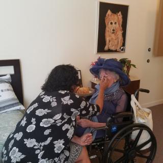 A caregiver assists an elderly person in a wheelchair within a home setting.