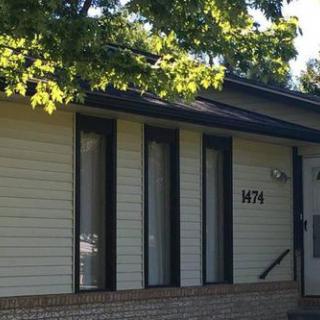 A residential house with a light exterior and narrow windows, partially shaded by trees.