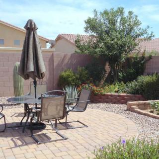A peaceful backyard patio with a table, chairs, and an umbrella surrounded by well-maintained garden landscaping.