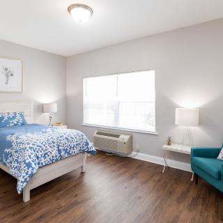 A well-lit modern bedroom featuring a bed with patterned bedding, two lamps, and a comfortable chair.