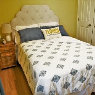 A cozy bedroom with a neatly made bed, featuring a quilt and decorative pillows, next to a wooden nightstand with a lamp.