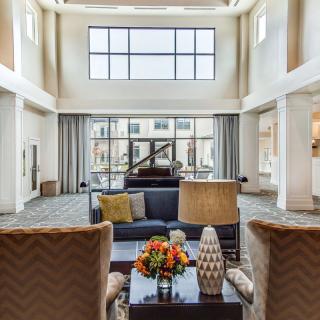 A spacious and elegantly designed living room with modern furniture, featuring a high ceiling and large windows that allow natural light to fill the space.