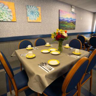 A neatly set dining table with a floral centerpiece and artwork on the walls.