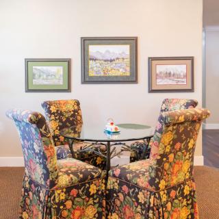 A cozy dining area featuring floral-patterned chairs around a glass table, complemented by framed artwork on the wall.