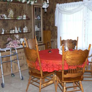A cozy dining room with a red tablecloth, wooden chairs, and decorative items in a cabinet.