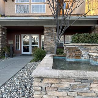 The entrance of a building with a stone fountain and landscaped pathway.