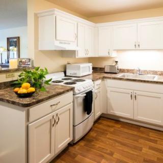 A modern kitchen with white cabinets and wooden flooring, featuring essential appliances and countertop decor.