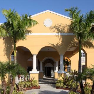 A tropical building with a yellow facade and palm trees at the entrance.