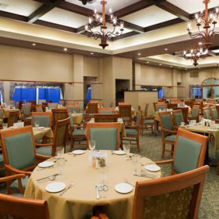 An elegant restaurant dining room with neatly arranged tables and chandeliers overhead.