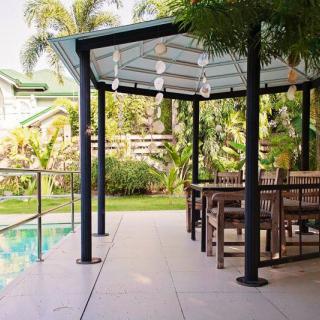 A modern outdoor patio area with a pergola, wooden furniture, and a view of a lush garden by the poolside.