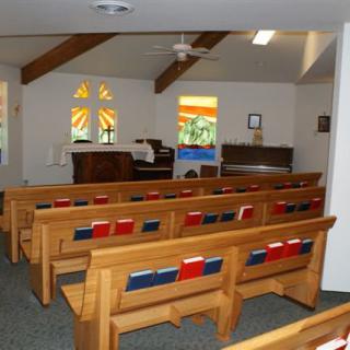 Interior view of a church sanctuary with wooden pews and stained glass windows.