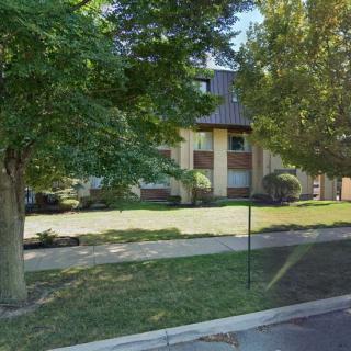A suburban house surrounded by lush trees and a well-kept lawn on a sunny day.
