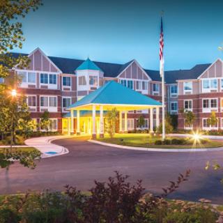 A beautifully illuminated hotel entrance at dusk, showcasing modern architecture and well-maintained landscaping.