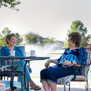 Two people enjoying a conversation on a patio by the lake.