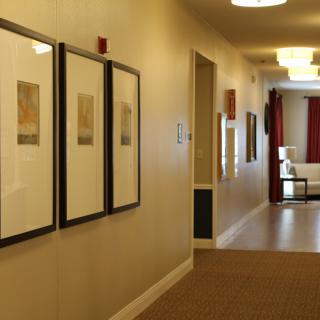 A hallway with framed artwork on the walls and a glimpse of furniture in the adjacent room.
