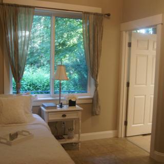 A cozy bedroom with a window view, featuring a bed and a nightstand with a lamp.