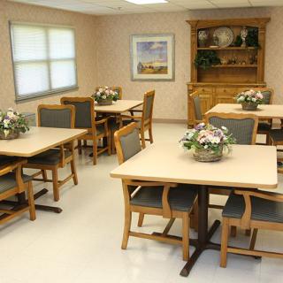 A neatly arranged dining room with tables and chairs, decorated with floral centerpieces.
