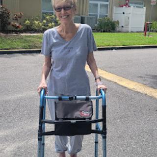 An elderly woman using a walker to assist her while walking outdoors.