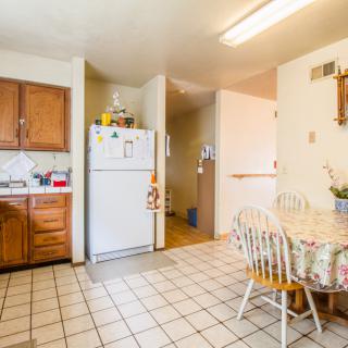 A cozy kitchen and dining area with wooden cabinets, a refrigerator, tile flooring, and a small table with chairs.