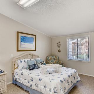A cozy bedroom with a bed adorned with patterned bedding, a framed picture above the headboard, and natural light filtering through a window.
