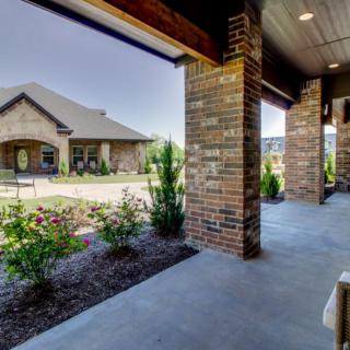 A view from the porch of a brick house overlooking a landscaped garden area.