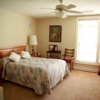 A cozy bedroom with a double bed, lamp, and large window allowing natural light.