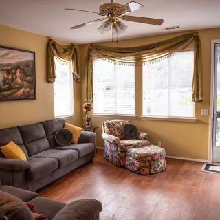A cozy living room with a gray sofa, floral armchair, and large windows letting in natural light.