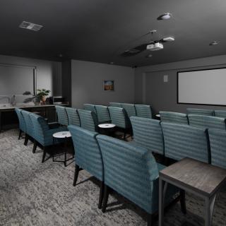 A cozy theater-style room with teal seating arranged in rows facing a large projector screen.