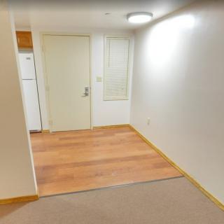 A narrow apartment interior with wood flooring and a view into the kitchen area.